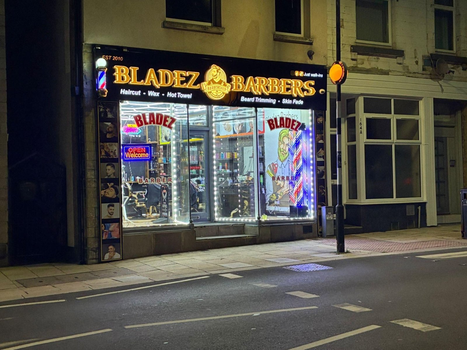 Bladez Barbers at night: the gold lit sign, windows edged with LED lights and an OPEN sign